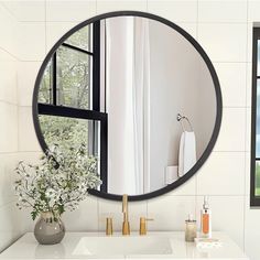 a bathroom with a round mirror on the wall and a vase filled with flowers in front of it