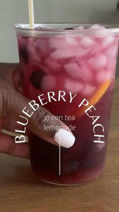 a hand holding a cup filled with blueberry peach tea