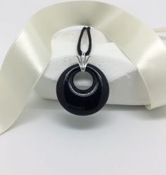 "Every woman needs a little black pendant like this one for sparkle and elegance. This fused glass circle pendant is 1.3\" round and hangs from a sterling silver fan shaped bail which extends .3\" above the pendant. The pendant hangs from a 24\" black satin cord knotted at the ends. All jewelry comes in a gift box tied with ribbon. (Packaging is made of recycled material.) I will add a gift card with your message if you ask at checkout. I have designed and created jewelry in my Connecticut home Black Donut, Ribbon Packaging, Glass Circle, Satin Noir, Fused Glass Pendant, Black Pendant, Circle Pendant, Glass Pendant, Style Moderne