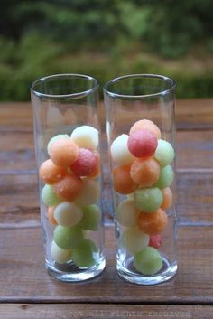 two glasses filled with fruit sitting on top of a wooden table