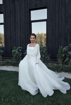 a woman in a white dress is sitting on the grass near some windows and looking at the camera