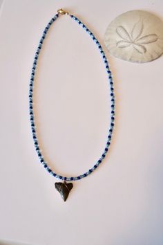 a necklace with blue beads and a small bead on it next to a sand dollar