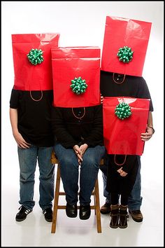 three people sitting on a chair with red bags over their heads and presents wrapped around them