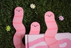 two pink worms are standing next to each other on the grass with flowers in the background