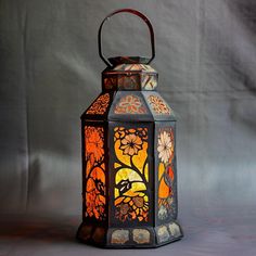 a decorative lantern with flowers and leaves painted on the side, sitting against a gray background