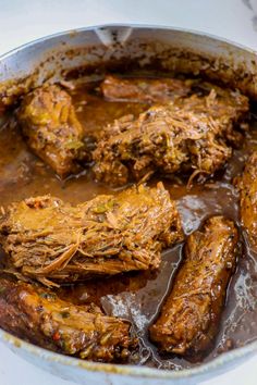 some meat and sauce in a pot on a stove top with a white table cloth