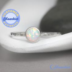 "This delicate Sterling Silver Opal Promise Ring features a 6 mm cabochon that has been carefully set in a highly polished fine silver bezel. The band is made of a sturdy round Sterling Silver wire that has been given a hammer texture, then carefully polished for a bright finish. Our setting process involves carefully tightening the fine silver bezel down around the stone, then beveling at the edge of the bezel to further compress the silver, creating a water-tight seal with no stone movement. T Silver Opal Birthstone Ring Gift, Silver Opal Stackable Rings As Gift, Opal Birthstone Ring As A Gift, Opal Gemstone Stackable Round Rings, White Opal Stackable Round Rings, Opal Gemstone Stackable Rings, Sterling Silver Opal Ring With Bezel Setting As Gift, White Opal Stackable Rings, Gift Opal Ring With Bezel Setting In Sterling Silver