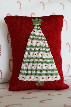 a knitted christmas tree pillow sitting on top of a bed next to a red pillow