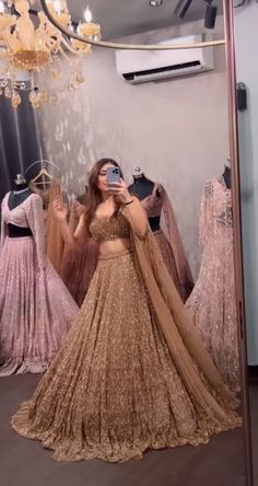 a woman taking a selfie in front of a mirror wearing a gold lehenga