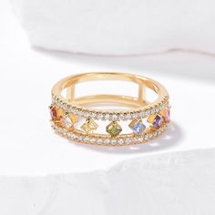 a gold ring with multicolored stones and diamonds on the inside, sitting on a white surface