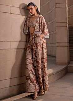 Embrace the elegance with the Brown Floral Applique Pant Cape set, the epitome of refined sophistication. The ensemble features a plunging brown blouse crafted from chikankari fabric, intricately adorned with shimmering pearls and sequin embroidery that beautifully catches the light. Teamed with a jaal organza cape that showcases delicate applique embroidery, this set is further embellished with sparkling pearls, adding a luxurious touch. The look is completed with matching organza pants, offering a graceful flow and cohesive aesthetic. This ensemble is a perfect indo western blend of traditional craftsmanship and modern design, making it an ideal choice for Mehndi, weddings, or festive occasions. Composition : Blouse - Chikankari, Cape and Pants - Organza Care: Dry Clean Only and Vacuum S Glamorous Silk Sets For Festive Season, Glamorous Silk Sets For Reception, Glamorous Silk Sets For Designer Wear, Glamorous Silk Designer Wear Sets, Glamorous Silk Set With Dupatta, Elegant Traditional Drape Pant Set For Diwali, Glamorous Festive Silk Sets, Elegant Pant Set With Traditional Drape And Zari Work, Elegant Party Pant Set With Traditional Drape