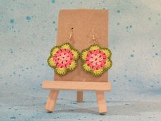 a pair of pink and green crocheted flower earrings sitting on top of a wooden stand