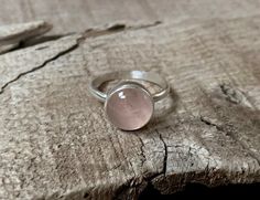 A beautiful round pink rose quartz sits in sterling silver with a handmade ring band from sterling silver half dome wire. Choose from either a simple setting or a more floral scallop setting. The rose quartz cabochon is 11mm in size. Rose quartz is a stone that promotes healing, love, and attraction. It can draw love to the the wearer, help heal from heartbreak, and help sustain feelings of love and romance. Made to order, stones vary with slight differences in color, lines, etc. Pink Moonstone Sterling Silver Ring For Anniversary, Pink Sterling Silver Moonstone Promise Ring, Round Rose Quartz Promise Ring, Round Rose Quartz Rings For Anniversary, Rose Quartz Round Rings For Anniversary, Adjustable Round Rose Quartz Jewelry, Rose Gold Moonstone Ring In Sterling Silver, Rose Gold Sterling Silver Moonstone Ring, Rose Quartz Anniversary Rings