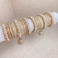 Large stack of luxurious Heavy Pearl & Antique Gold bangles with cream and pale gold shades finished with jhumka drops and Clear stonework. The perfect stack for any Bride or those wanting to make a statement. Ready to Ship as pictured. White Bollywood Bracelet With Stone Work, Bohemian Cream Bangle Jewelry, Bohemian Cream Bangle, Adjustable Gold Bangle With Gota Work, Cream Bangle Jewelry For Wedding, Cream Bangle For Wedding, Traditional Cream Jewelry For Wedding, Bollywood Style White Bangle Bracelet, Adjustable Traditional Cream Jewelry