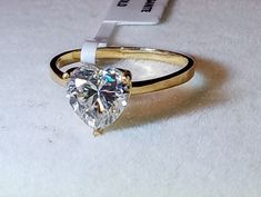 a heart shaped diamond ring sitting on top of a white table next to a tag