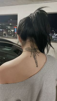 the back of a woman's neck with a cross tattoo on her left shoulder