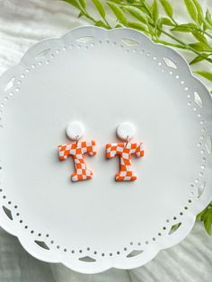 two orange and white checkered earrings sitting on top of a plate