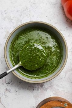 a bowl filled with green pesto next to tomatoes