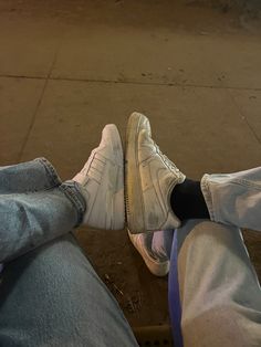 two people are sitting on the curb with their feet up and one is wearing white sneakers