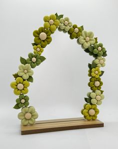 an arch made out of green and yellow flowers on a wooden stand with white background