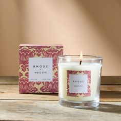 a candle sitting on top of a wooden table next to a pink and white box