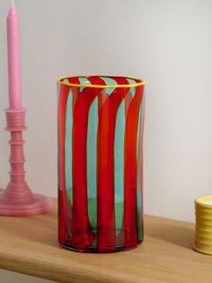 a red and blue glass sitting on top of a wooden table next to a pink candle