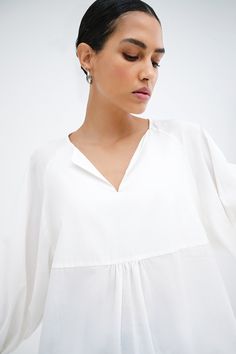 Our Kissena Top is your escape to a world of polished ease. A babydoll silhouette from lightweight European cotton voile, this billowing beauty features a notched neckline and raglan sleeves that flow down the arm before gathering into a cuff. Precisely tailored for effortless outfitting, Kissena is a refreshing take on a versatile daily essential. | Astrid, in off white, is 5'9" (175 cm) tall, wearing size XS. Yada, in black, is 5'9" (175 cm) tall, wearing size XS. Total length from the front i White Billowy Blouse For Summer, Billowy White Blouse For Summer, Billowy White Summer Blouse, White Flowy Breezy Blouse, Breezy Flowy White Top, Flowy Summer Blouse For Daywear, Flowy Breezy Tops For Daywear, White Flowy Blouse For Daywear, Effortless White Blouse For Daywear