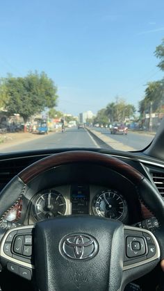 the dashboard of a car on a road with trees and buildings in the back ground