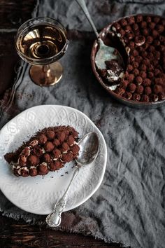 a piece of chocolate cake on a plate next to a glass of wine and spoon