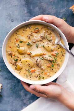 two hands holding a bowl of chicken and dumpling soup on a blue tablecloth