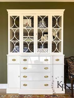 a white china cabinet sitting on top of a wooden floor next to a zebra print rug