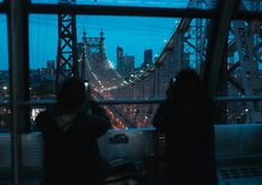 two people standing in front of a window looking out at the city lights and bridge