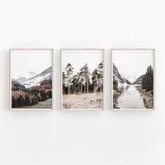 three framed photographs hang on the wall above a white table in front of mountains and trees