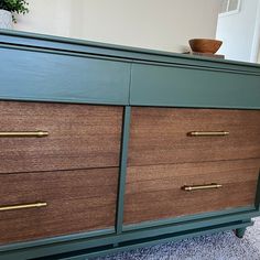 a green and brown dresser with brass handles on carpeted floor next to potted plant