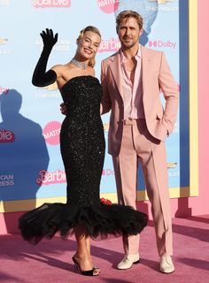 a man and woman standing on a pink carpet in front of a sign that says barbie