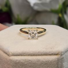 a diamond ring sitting on top of a white box with flowers in the back ground