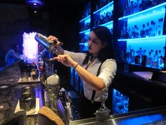 a woman is pouring something into a glass at the bar with blue lights behind her