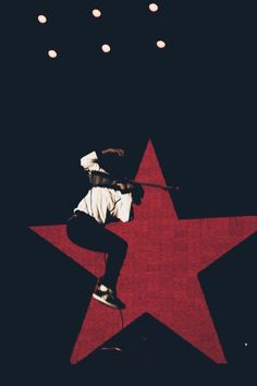 a man on a skateboard in front of a red star with lights hanging from the ceiling