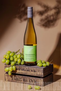 a bottle of wine sitting on top of a wooden crate filled with grapes and green leaves