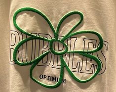 a white t - shirt with a green clover on it's chest and the words pubbitfests optimium written in black