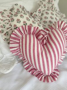 a heart shaped pillow sitting on top of a bed covered in pink and white striped fabric