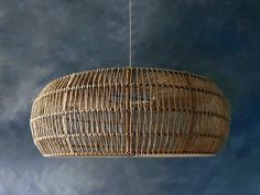 a hanging light made out of wicker on a blue wall with clouds in the background