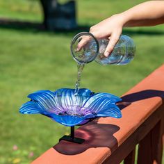 a person is pouring water into a blue flower shaped glass vase on a wooden fence