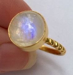 This Awesome Rainbow Moonstone, 12mm Round, Natural Gemstone is set in a Lovely Gold plated, Sterling Silver Ring.  This Beautiful Moonstone has an Awesome blue flash of color with faint striations, and shades of color, that will appear and disappear, according to the light source, (giving it a mystical essence.) As Moonstone is a natural gemstone, that man has not been able to recreate, you will never see two that are exactly alike. This ring would be a great gift for a lady of any age, and Moonstone is also used as the June birth stone. Gold Moonstone Cabochon Ring, Gold Moonstone Ring With Natural Stones, Gold Moonstone Ring With Stone Setting, Gold Moonstone Birthstone Ring With Round Stone, White Ethical Round Gemstones, Round Moonstone Gemstones, White Round Moonstone Gemstones, Round Moonstone Gemstones For Anniversary, Round Moonstone For Anniversary