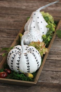 two white pumpkins sitting in a wooden box with greenery on the side and other decorations around them