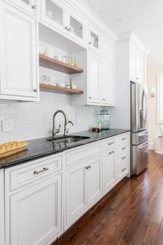 a kitchen with white cabinets and black counter tops, wood flooring and stainless steel appliances