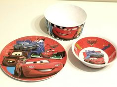 two plates with cars printed on them are next to a bowl and cup sitting on a table