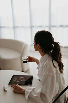 a woman sitting at a table with a glass of wine in her hand and an electronic tablet on the table