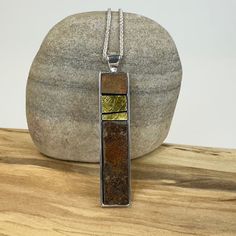 a silver and gold pendant sitting on top of a wooden table next to a rock