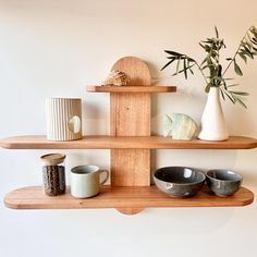 three wooden shelves with bowls and vases on them, one shelf has two plants